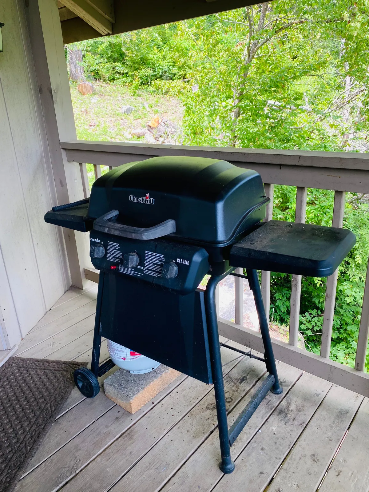 A view of the deck with a prominent propane BBQ grill, additional seating, and greenery all around. The setting is casual and set up for outdoor meals, celebrations, or relaxed cookouts, highlighting the versatility of the outdoor space.
