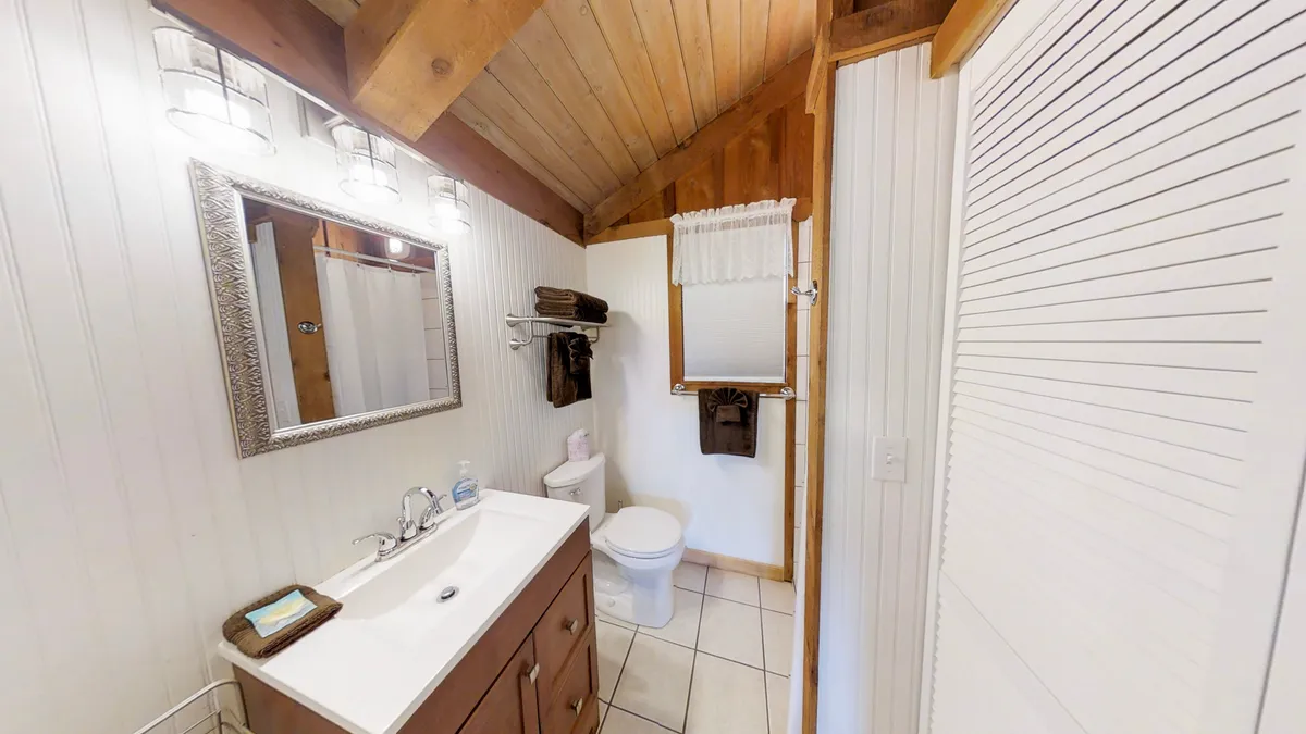 A serene bathroom scene featuring a modern vanity with a mirror, exposed wooden beams above, and a tiled floor. The atmosphere is calm and inviting, ideal for relaxation and personal care. The space evokes a sense of quiet retreat, perfect for unwinding after a day outdoors.