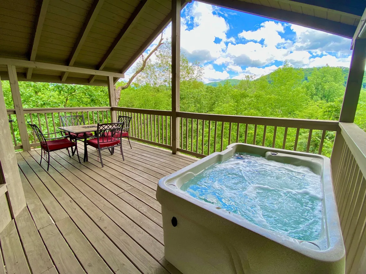 This image features the cabin’s outdoor deck, complete with a private hot tub, a dining table, and lush surrounding greenery. The deck overlooks the river, offering a tranquil view that highlights both relaxation and family togetherness. The scene captures opportunities for stargazing from the hot tub, morning yoga sessions, and evening meals with breathtaking views.